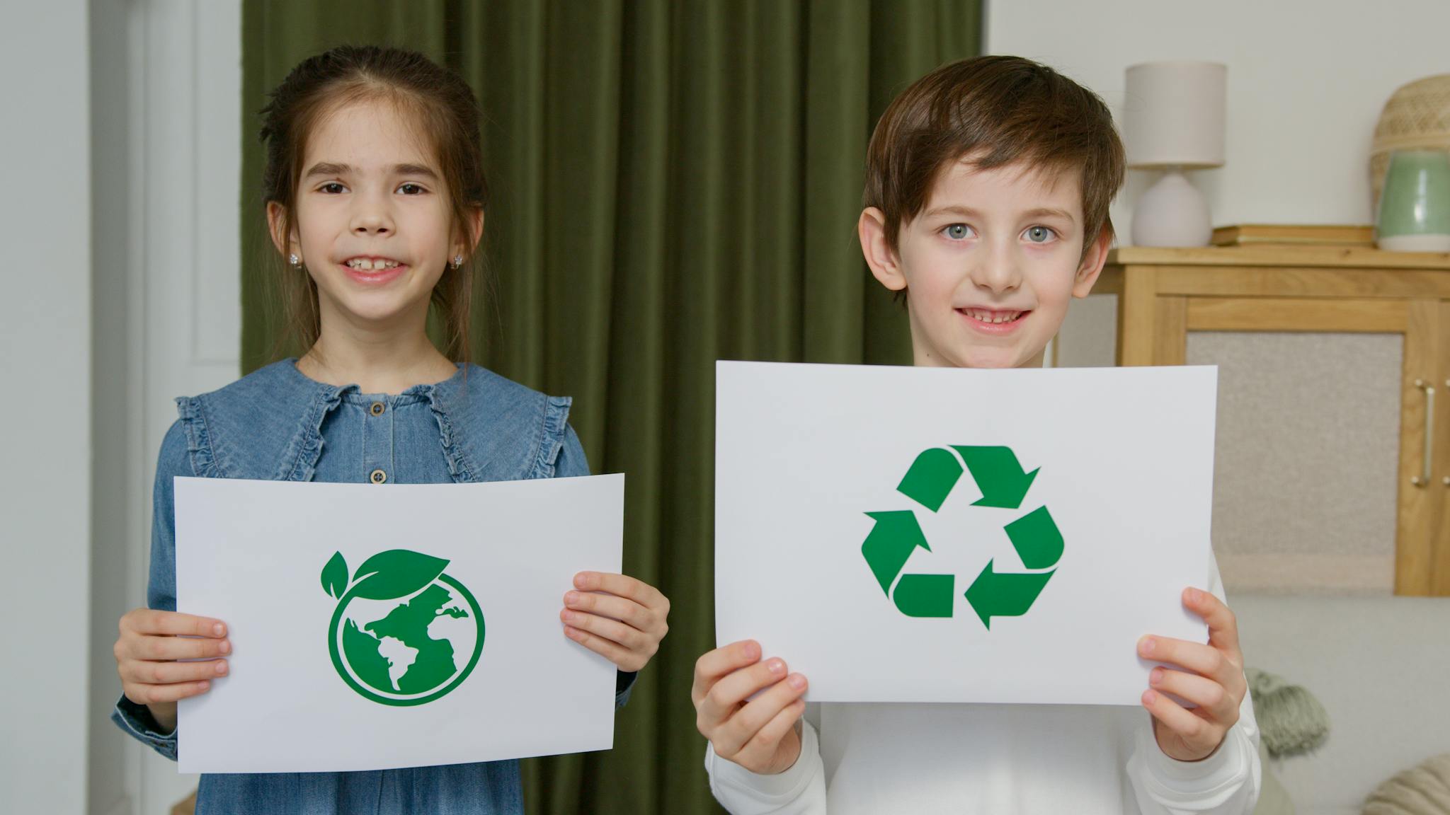 Two children holding eco-friendly signs indoors, promoting sustainability.